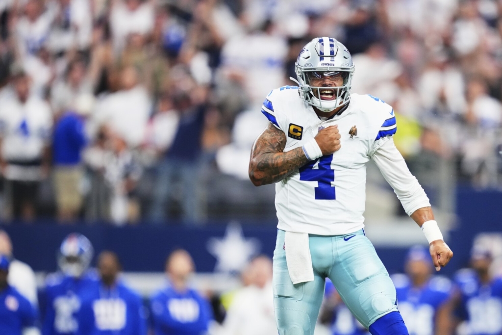 Dallas Cowboys football player celebrating on the field during an NFL game, wearing uniform with number 4, helmet, and tactical gear, emphasizing team spirit and game excitement.