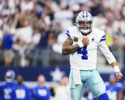 Dallas Cowboys football player celebrating on the field during an NFL game, wearing uniform with number 4, helmet, and tactical gear, emphasizing team spirit and game excitement.