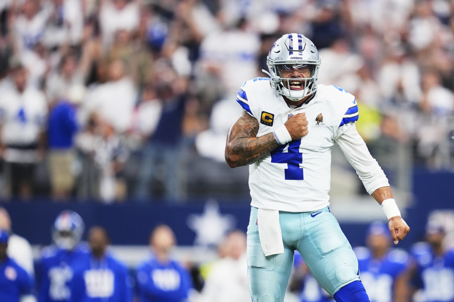 Dallas Cowboys football player celebrating on the field during an NFL game, wearing uniform with number 4, helmet, and tactical gear, emphasizing team spirit and game excitement.